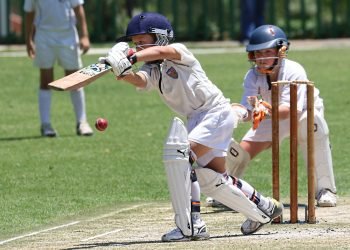 Young cricketers playing with focus and skill on a sunny outdoor field.